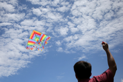 An Asian young man is enjoying kite flying during his leisure time.