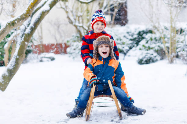 istock Two kid boys having fun sleigh ride during snowfall. Children sledding on snow. siblings riding a sledge. Twins play outdoors. Friends sled in snowy winter park. Active fun for family vacation 1344534378