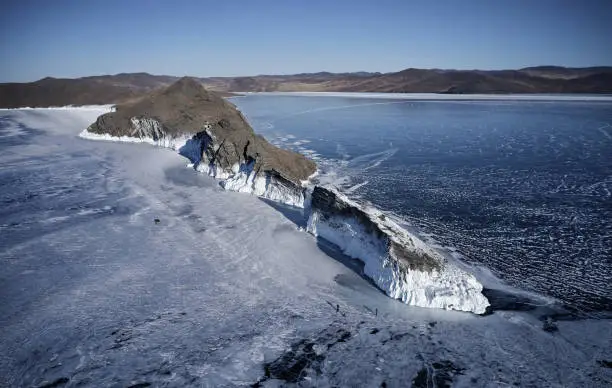 Photo of Frozen Lake Baikal, cape Horin-Irgi of Olkhon Island. Beautiful winter landscape with clear smooth ice near rocky shore. The famous natural landmark Russia. Blue transparent ice with deep cracks