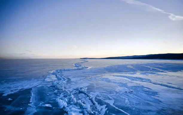 Photo of Frozen Lake Baikal, Lake Baikal hummocks. Beautiful winter landscape with clear smooth ice near rocky shore. The famous natural landmark Russia. Blue transparent ice with deep cracks