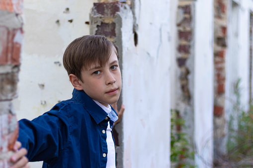 A fashionably dressed guy in a blue shirt stands against the background of an old destroyed brick wall. Close-up. Selective focus. Portrait