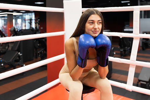 Sporty woman in boxing gloves resting while sitting in the ring