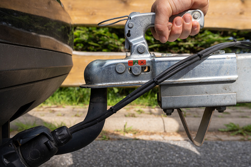 woman's hand checks the fixation of the trailer closed hitch lock handle on the towing ball towbar of the car closeup, the safety of driving with a trailer on the road