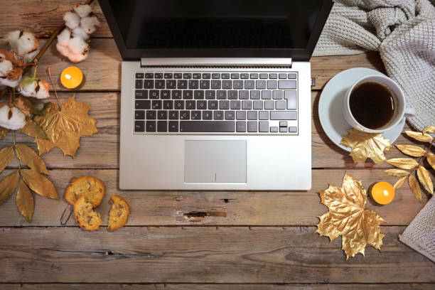 istock laptop computer and coffee cup on a rustic wooden table decorated with gold painted autumn leaves and candles, cozy home office, flat lay from above, copy space 1344555340