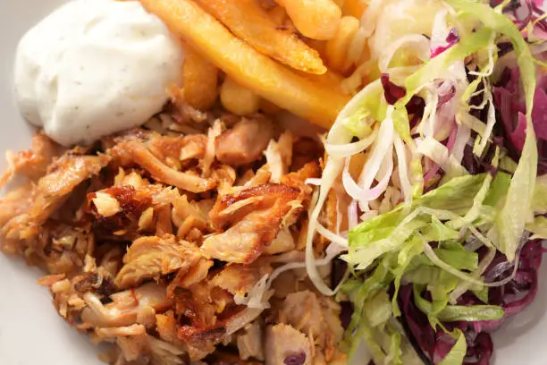 Roasted doner kebab chicken meat with french fries, salad and tzatziki dip, high angle view from above, full frame close-up shot, selected focus, narrow depth of field