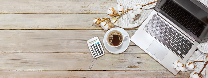 laptop computer, coffee cup and calculator on a rustic wooden table with cotton branches, business and finance accounting in the home office in autumn, panoramic format, copy space, flat lay from above, selected focus