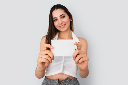 Young brunette woman is holding a blank note paper for mock up use. Silent communication concept. High quality photo