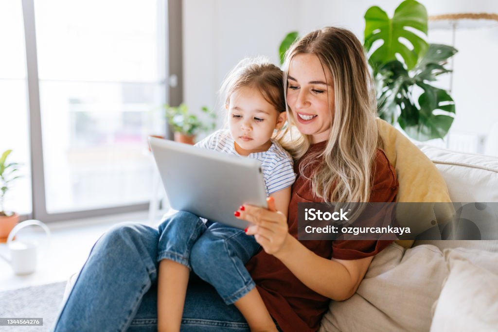 Mother and daughter using a digital tablet together Mother and daughter using a digital tablet together. They are sitting on the sofa at home. The daughter is sitting on his mothers lap. Very hapy and smiling. Close up with Tight crop Digital Tablet Stock Photo