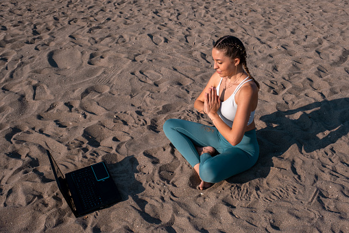 young woman doing online yoga training at the beach