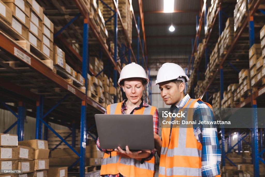 Logistic worker staff colleague in safety suit holding computer laptop working in a warehouse store Warehouse Stock Photo