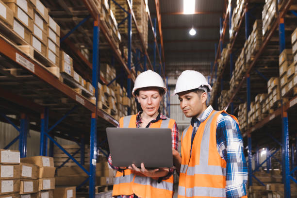 logistic worker staff colleague in safety suit holding computer laptop working in a warehouse store - hardware store fotos imagens e fotografias de stock