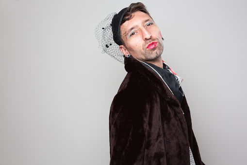 Mid adult man with black beard, dressed as  woman, wearing  fake fur coat, a shirt with leopard pattern, he has colorful makeup applied, he is making a kiss