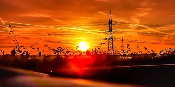 Orange sunrise in autumn next to the motorway in Germany with electricity pylon in a field