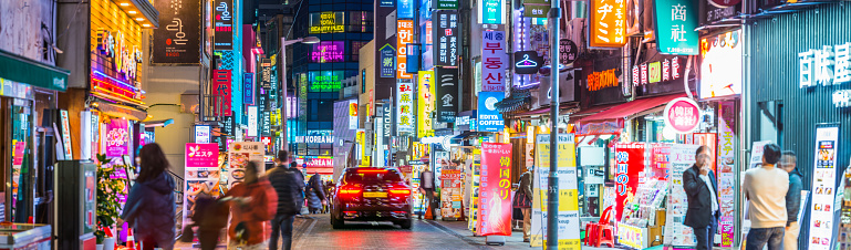 Crowds of shoppers along the streets of Myeong-dong overlooked by the neon lights of stores in the heart of Seoul at night, South Korea’s vibrant capital city.