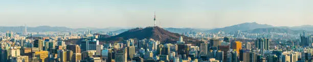 Aerial panorama over the crowded highrise cityscape of central Seoul nestled between the green mountains that surround South Korea’s vibrant capital city.
