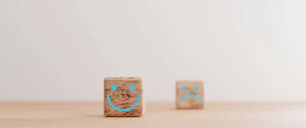 Photo of Focus of Smile face print screen on wooden cube block and defocus sadness face on dark side for customer service evaluation and emotion mindset concept by 3d render.