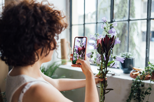 An unrecognizable female florist taking a picture of her flowers using a mobile phone