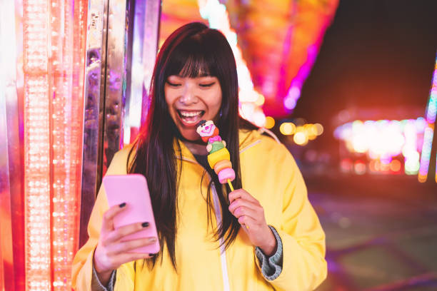 Asian girl taking using mobile phone in amusement park - Happy woman having fun with new trends smartphone apps - Youth millennial people generation and social media addiction concept stock photo