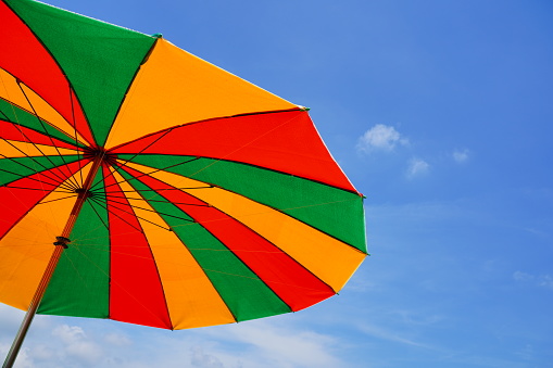 Three colorful umbrellas - red, yellow and green - fly in the blue sky