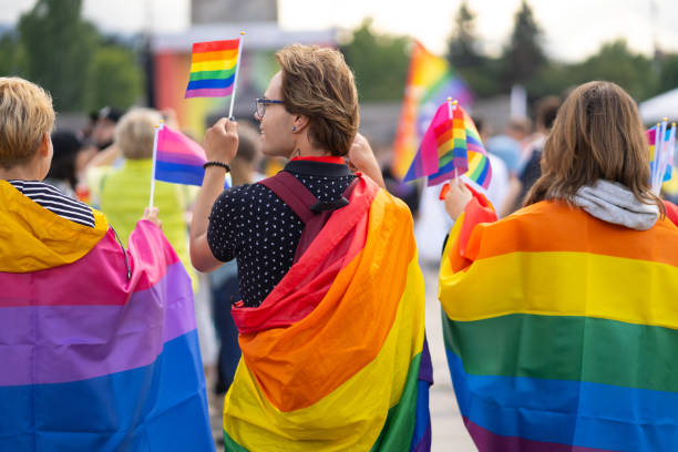 envuelto en banderas de bandera bisexual y orgullo, este trío está viendo un evento del orgullo gay - gay pride flag gay pride gay man homosexual fotografías e imágenes de stock