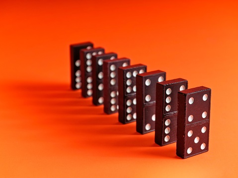 Old wooden dominoes in a row ready to be tipped over on a bright orange background. A classic game from the past that is also used for making a train or chain reaction of toppling over.