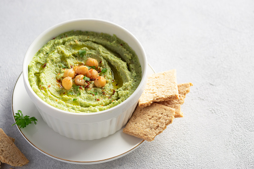 close-up white bowl with avocado hummus with chickpeas, parsley, spices and crackers on gray background. Clean eating, dieting. side view. place for text.