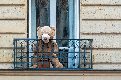 A huge teddy bear sits on a balcony and looks out over the street