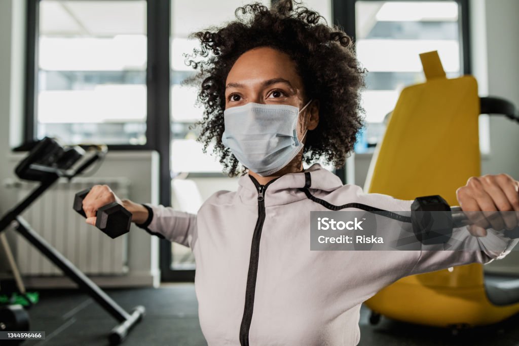 Woman doing exercises with a face mask Close up of a young woman with a face mask, doing exercises with dumbbells Exercise Class Stock Photo