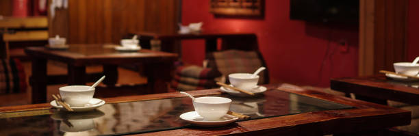 White ceramic tableware and bamboo chopsticks on wooden table in traditional Yunnan cuisine restaurant with red interior wall.
Yunnan cuisine, alternatively known as Dian cuisine, is an amalgam of the cuisines of the Han Chinese and other ethnic minority groups in Yunnan Province in southwestern China. Many Yunnan dishes are quite spicy, and mushrooms are featured prominently. Flowers, ferns, algae and insects may also be eaten.