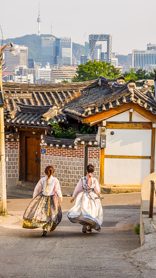 Seoul, South Korea - June 21, 2017: Two young women in colorful traditional wear - hanbok walking down the street in Bukchon Hanok Village in Seoul.