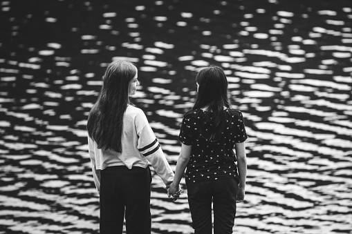 Two teenage cousins together hand in hand, looking the turquoise river water. Friendship concept. Black and white version.