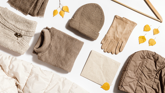 Autumn warm clothing beige colored, folded knitted wear, hat, scarf, gloves, sweater with craft paper for copy space. Creative Flat lay from female fashion autumnal outerwear for cold weather in fall season.