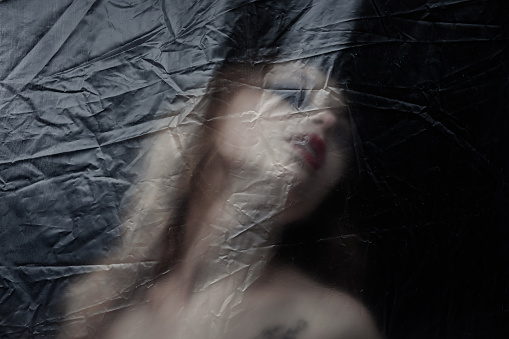 Young beauty sad woman trapped behind a plastic sheet as protection against COVID-19. Nicely fits for book cover