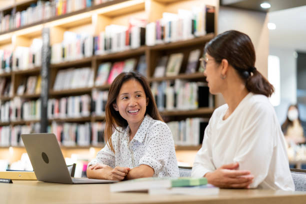 zwei erwachsene frauen, die zusammen in der bibliothek studieren - adult student women mature adult library stock-fotos und bilder