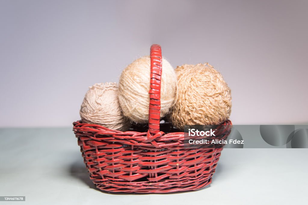 Beige balls of wool inside a wicker basket Beige balls of wool of different sizes inside a wicker basket on a white background Knitting Needle Stock Photo