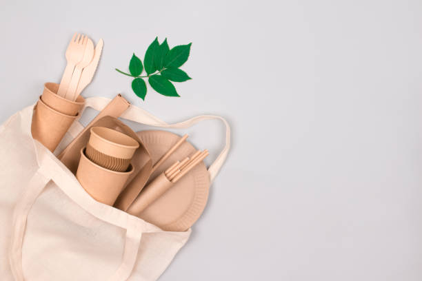 istock Eco-friendly tableware - kraft paper cups and containers in white cotton bag on gray background with copy space for text. Street food take away paper packaging - cups, plates, straws 1344613123