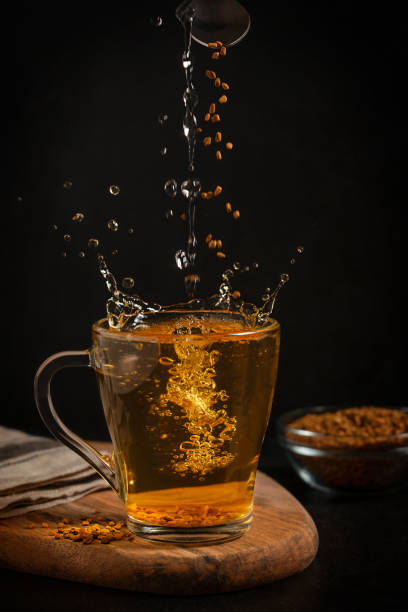 Glass cup of hot helba golden tea with splashes and fenugreek seeds used as healthy drink in Egypt Helba or golden tea made of fenugreek annual plant seeds served in glass cup with splashes and grains falling served on wooden cutting board against black background used in local medicine of Egypt fenugreek stock pictures, royalty-free photos & images