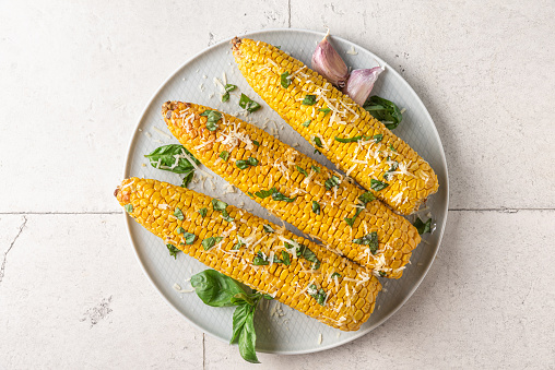 Corn cobs grilled and baked in a plate with parmesan cheese, garlic and basil. Top view. Healthy vegetarian food