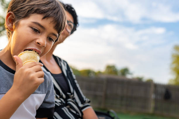 彼の隣に座っている彼の母親とアイスクリームを食べるかわいい若い男の子のクローズアップ。 - women eating ice cream indigenous culture ストックフォトと画像