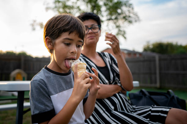 愛らしい男の��子は、母親が見て微笑みながらアイスクリームを食べます。 - women eating ice cream indigenous culture ストックフォトと画像