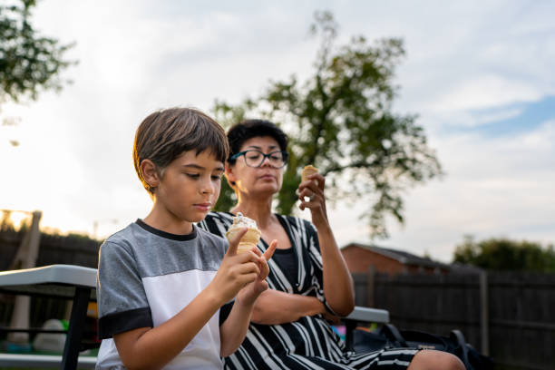 外に座っている間にアイスクリームコーンを食べているかわいい男の子と彼の母親。 - women eating ice cream indigenous culture ストックフォトと画像