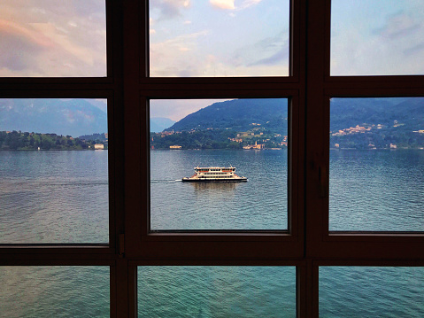 Lake Como, Italy - June 2019: Ferry on Lake Como viewed through the window frames of a lakeside hotel