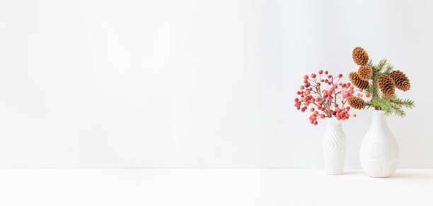 istock Home interior with decor elements. Small red apples in a vase and branches of spruce with cones on a light background 1344624162