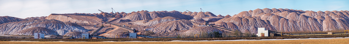 Panoramic view Salt mining site under blue bright sky. Large excavator machine and Huge mountains of waste ore in the extraction of potassium.
