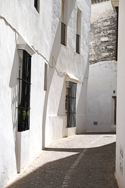 Empty street alley with white buildings, barred windows, Spanish traditional architecture, Arcos de la Frontera stock photo
