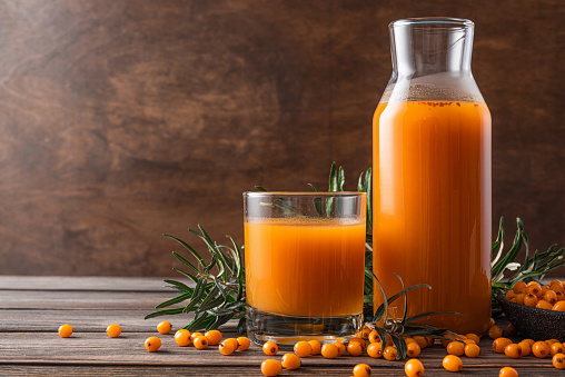 Sea buckthorn juice in glass jug and cup with fresh autumn berries on wooden background. Healthy antioxidant vitamin drink