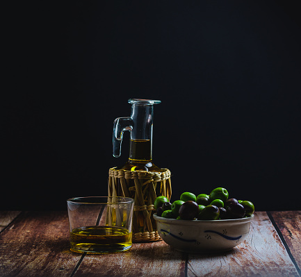 Still life of organic olives, and bottle of oil, on wooden table and black background, with natural light