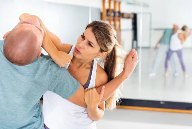 Young woman practicing elbow blow with male partner during self defense course in gym