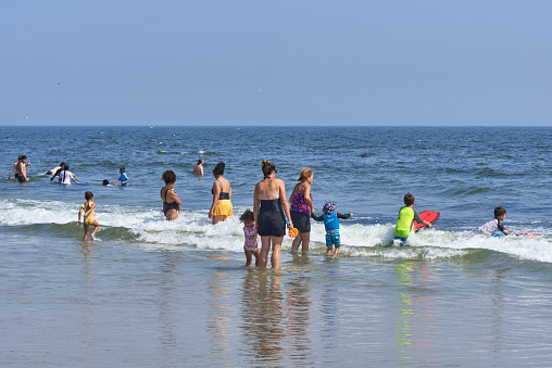 August 26, 2021: Beach goers enjoying the sun, sand and surf at Rockaway Beach, Queens, NYC on a hot summer day. Mothers and children wade in the surf.