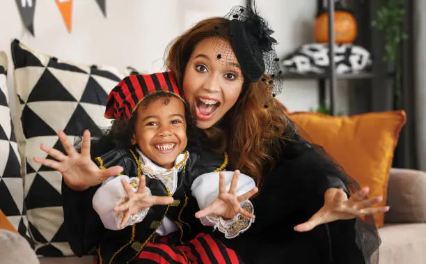 Photo of Joyful african american family mother and little boy son in Halloween costumes making scary gesture